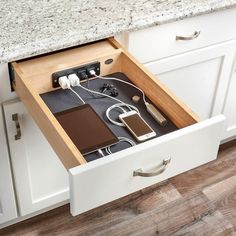 an open drawer in the middle of a kitchen with electronic devices and cords on it