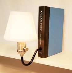 a lamp on a shelf next to a book and a light bulb that is plugged into the wall