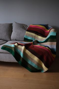 a couch with a blanket sitting on top of it next to a wooden floor in front of a gray wall