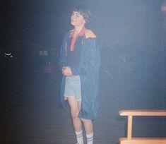 a young man standing in the dark with his coat over his shoulders and socks on