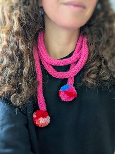 a woman with curly hair wearing a pink knitted scarf and red, white, and blue pom - pom necklace