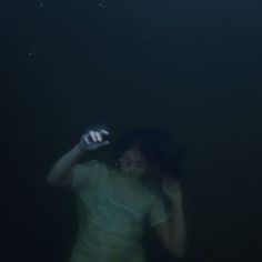 a woman standing in the water with her hand up to her head and holding an object above her head