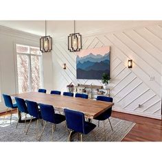 a dining room table with blue chairs in front of a large painting on the wall