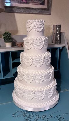 a three tiered white wedding cake sitting on top of a blue tablecloth covered floor