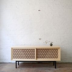 a white brick wall with a wooden sideboard and vase sitting on top of it