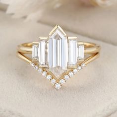 a gold ring with an emerald cut diamond surrounded by white diamonds on a beige background