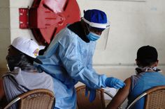 three people in protective gear sitting at a table and one person wearing a face mask