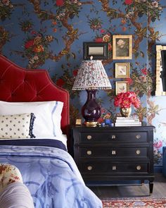 a bedroom decorated in blue and red with flowers on the wall, bed linens, lamps, and pictures