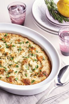 a casserole dish with cheese and herbs in it on a table next to silverware