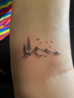 a small tattoo on the back of a woman's left arm, with trees and mountains in the background