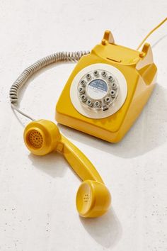 an old fashioned yellow telephone sitting on top of a white counter next to a cord