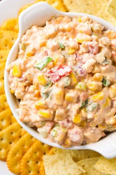 a white bowl filled with corn salad surrounded by crackers and chips on the side