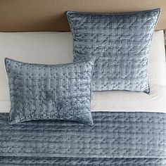 two blue pillows sitting on top of a bed next to a white pillowcase and headboard