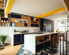 a kitchen with blue and yellow cabinets, white counter tops and wooden stairs leading up to the second floor