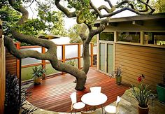 an outdoor deck with table, chairs and tree in the middle on top of it