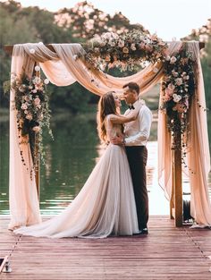 a bride and groom standing on a dock in front of an arch decorated with flowers