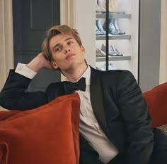 a young man in a tuxedo sitting on a couch with his hands behind his head