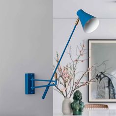 a blue wall light on the side of a white wall next to a vase with flowers