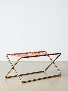 a small metal and leather bench sitting on top of a white floor next to a wall