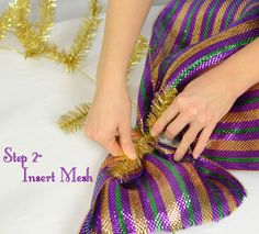 a woman is tying a purple and green ribbon on her skirt with gold tinsel