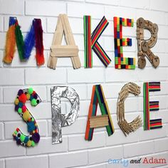 the letters are made out of wooden sticks and plastic beads on a white brick wall