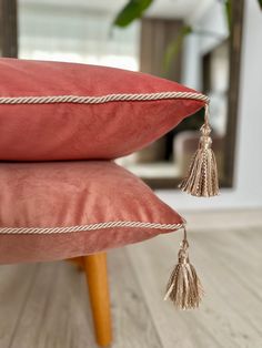 two red pillows with tassels on them sitting on a wooden floor next to a plant