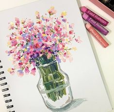 a drawing of flowers in a glass vase with markers on the table next to it