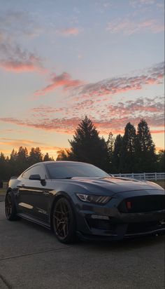 a black mustang parked in front of a fence with the sun going down behind it