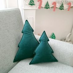 two green christmas trees sitting on top of a couch next to a wall with holiday decorations