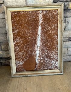 a framed cowhide print is shown in front of a brick wall