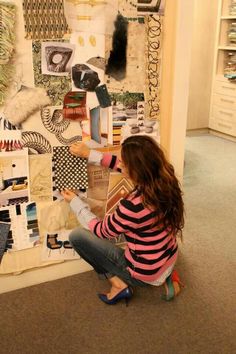 a woman sitting on the floor next to a wall covered in pictures