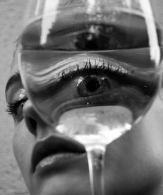 a woman's face is reflected in a wine glass with water pouring out of it