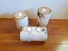 three white candles are placed in birch logs