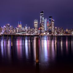 the city skyline is lit up at night with lights reflecting in the water and buildings