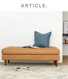 a tan leather bench sitting in front of a white wall with a book on it