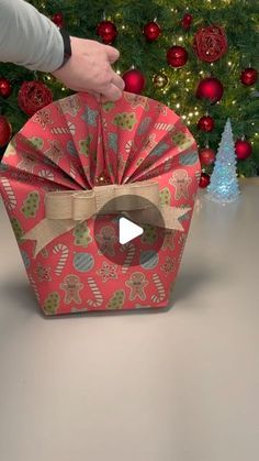 a person opening a christmas present box in front of a tree