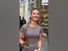 a woman is standing on the street holding a rose