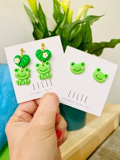 the frog earrings are being held up in front of a potted plant with flowers