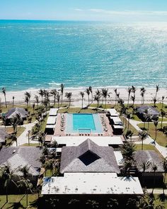 an aerial view of a beach resort with a swimming pool surrounded by palm trees and the ocean