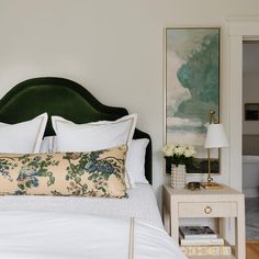 a green headboard in a bedroom with white bedding and flowers on the nightstand