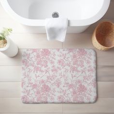 a bath mat with pink flowers on it next to a white sink and toilet paper