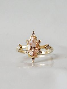 an engagement ring with a pink diamond and two white diamonds on the side, set in yellow gold