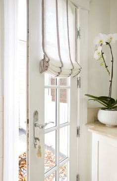 an open door with a white vase and flowers on the window sill next to it