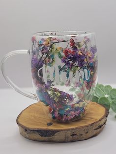 a glass coffee mug with the word hello on it sitting on a piece of wood