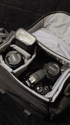 an open camera bag sitting on top of a black bed with its contents in it