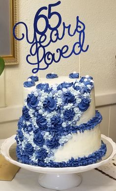 a blue and white cake with the number 65rd loved on top is sitting on a table