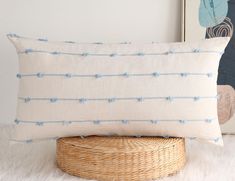 a white and blue pillow sitting on top of a wicker basket next to a painting