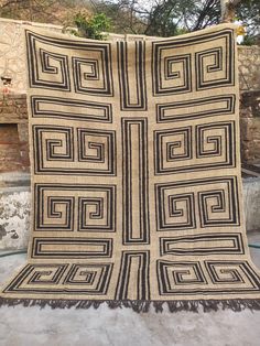 a black and white quilt on display in front of a stone wall with trees behind it