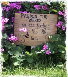 a sign that is in the grass with flowers around it and some words written on it