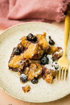 a white plate topped with blueberries and powdered sugar next to a yellow fork